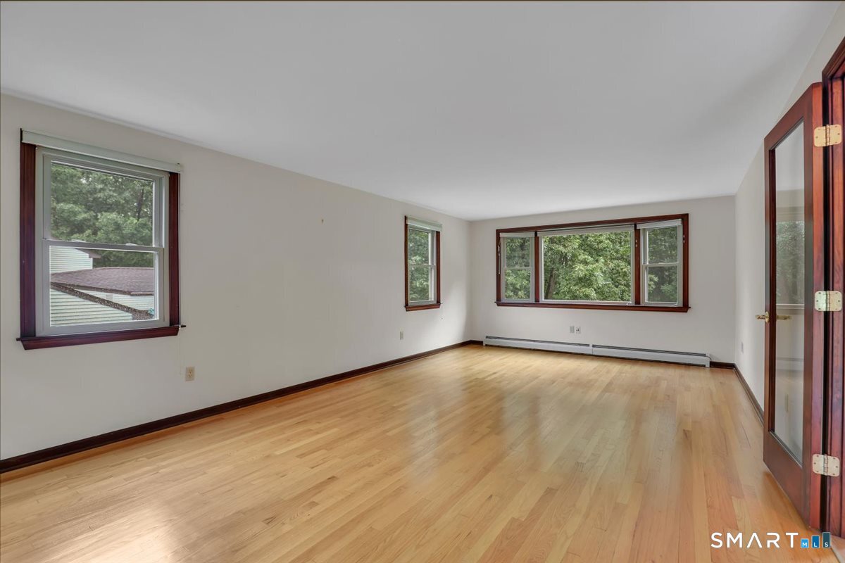 Empty room with hardwood floors, dark wood trim, and windows overlooking trees.