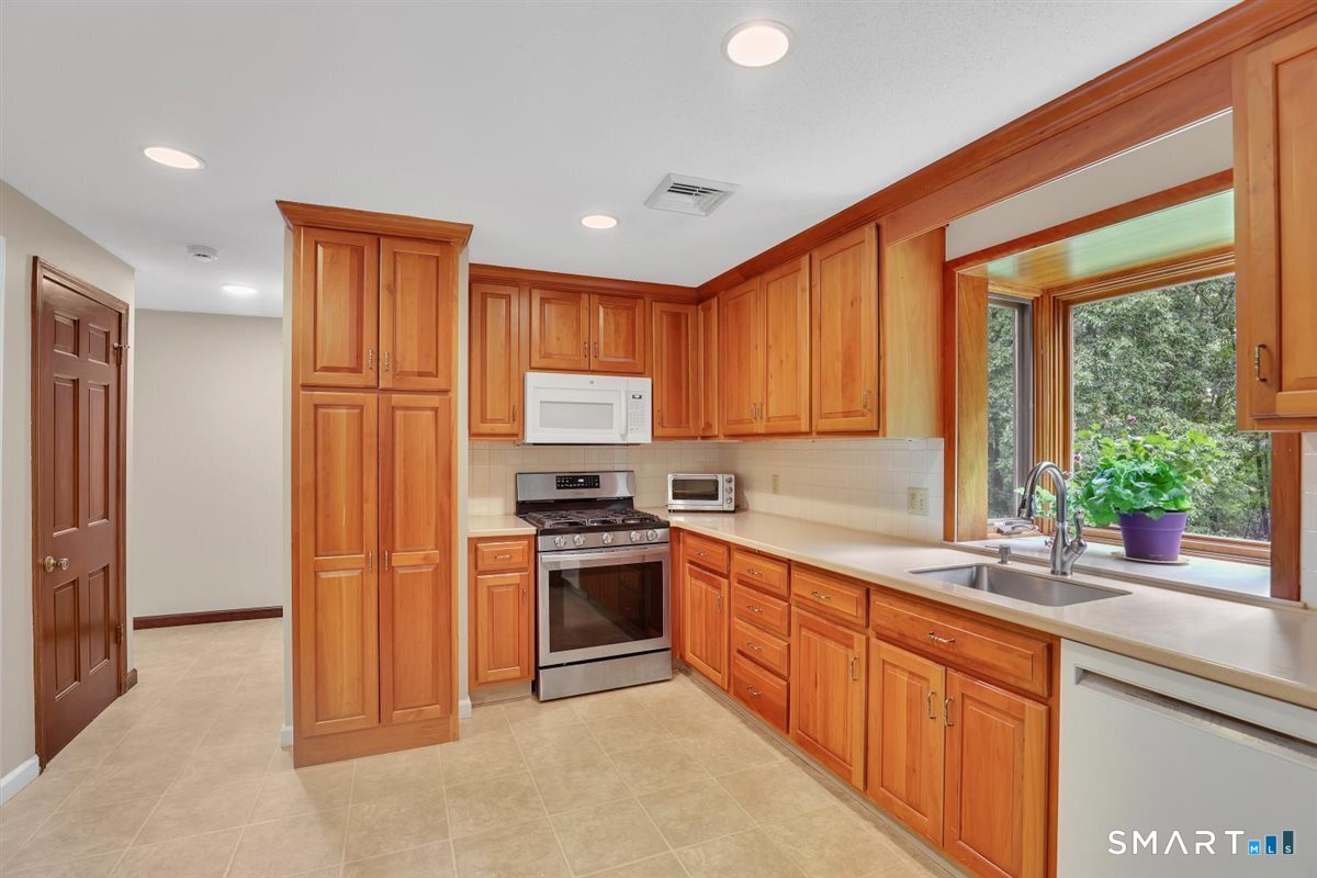 Kitchen with honey-toned cabinetry, stainless steel appliances, and a sink beneath a large garden-view window.