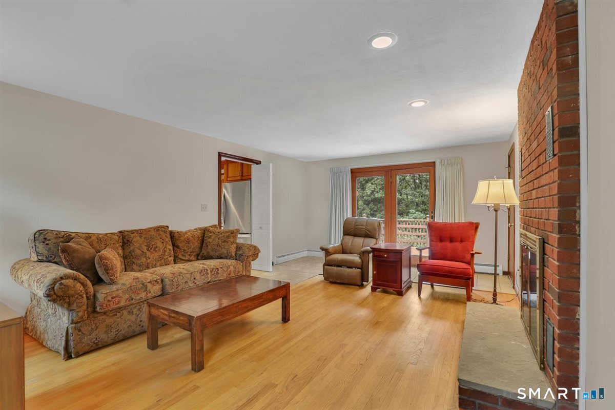 Living room with a brick fireplace, hardwood floors, and sliding glass doors overlooking trees.