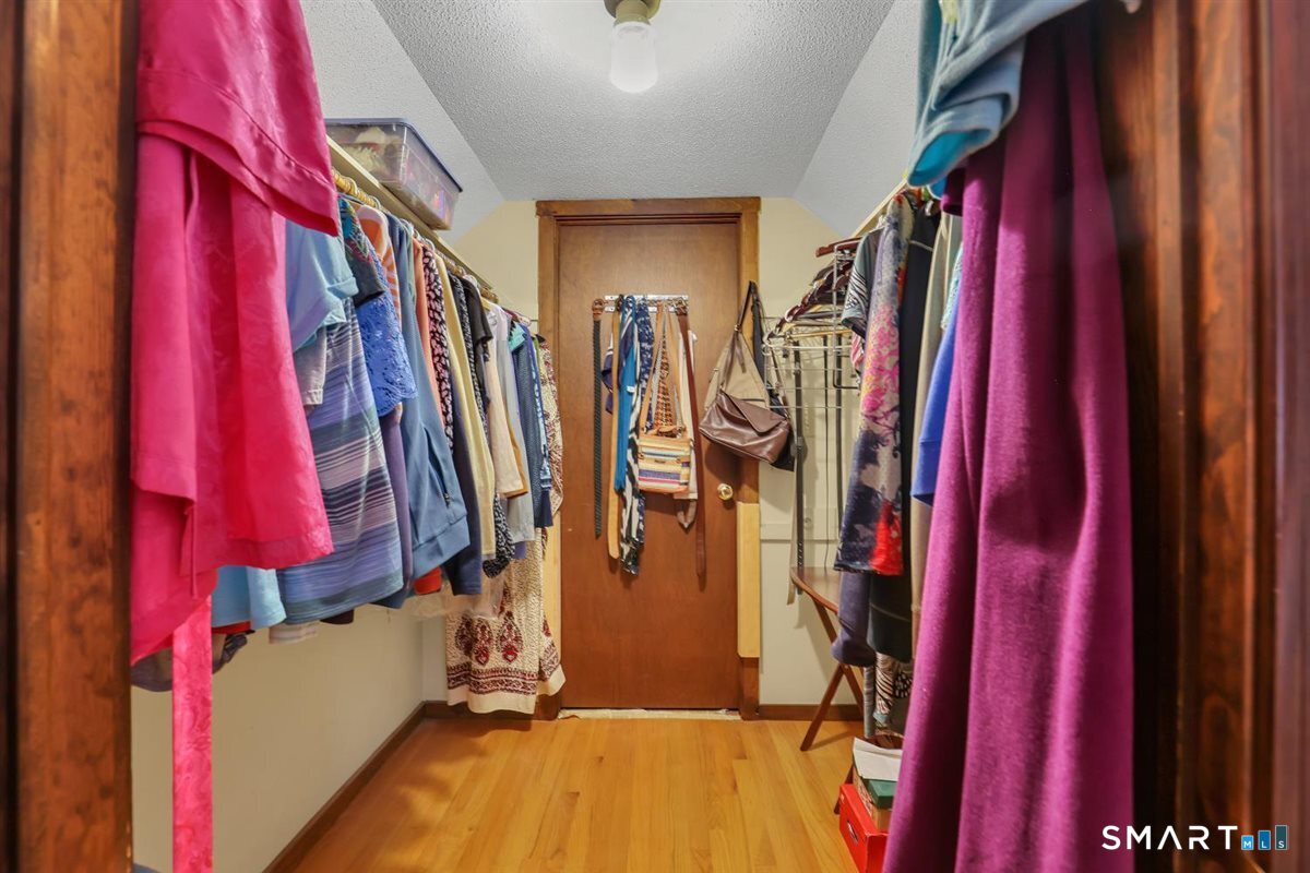 Walk-in closet with clothes lining both walls and hardwood flooring.