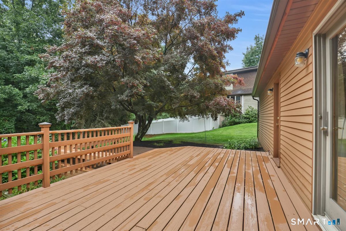 Wooden backyard deck with railing, mature trees, lawn, and a white privacy fence.