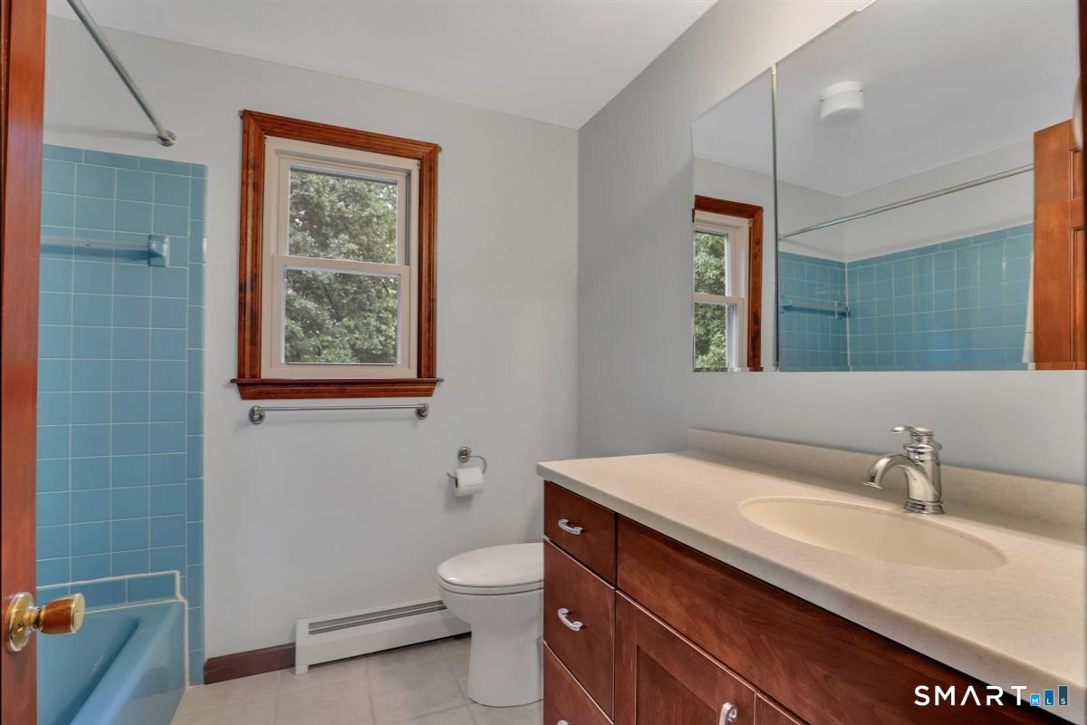 Bathroom with blue tiled tub and shower, wood-trimmed window, and wood vanity.