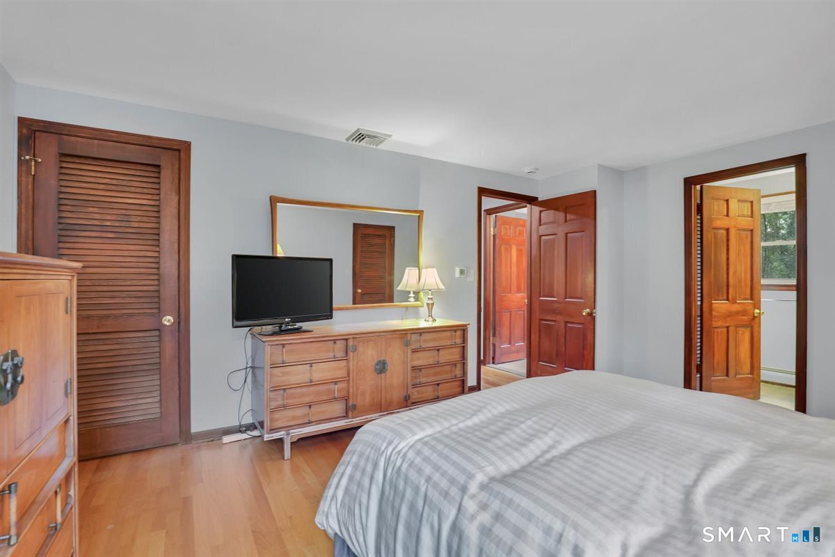 Bedroom with gray striped bedding, hardwood floors, and warm wood furniture.