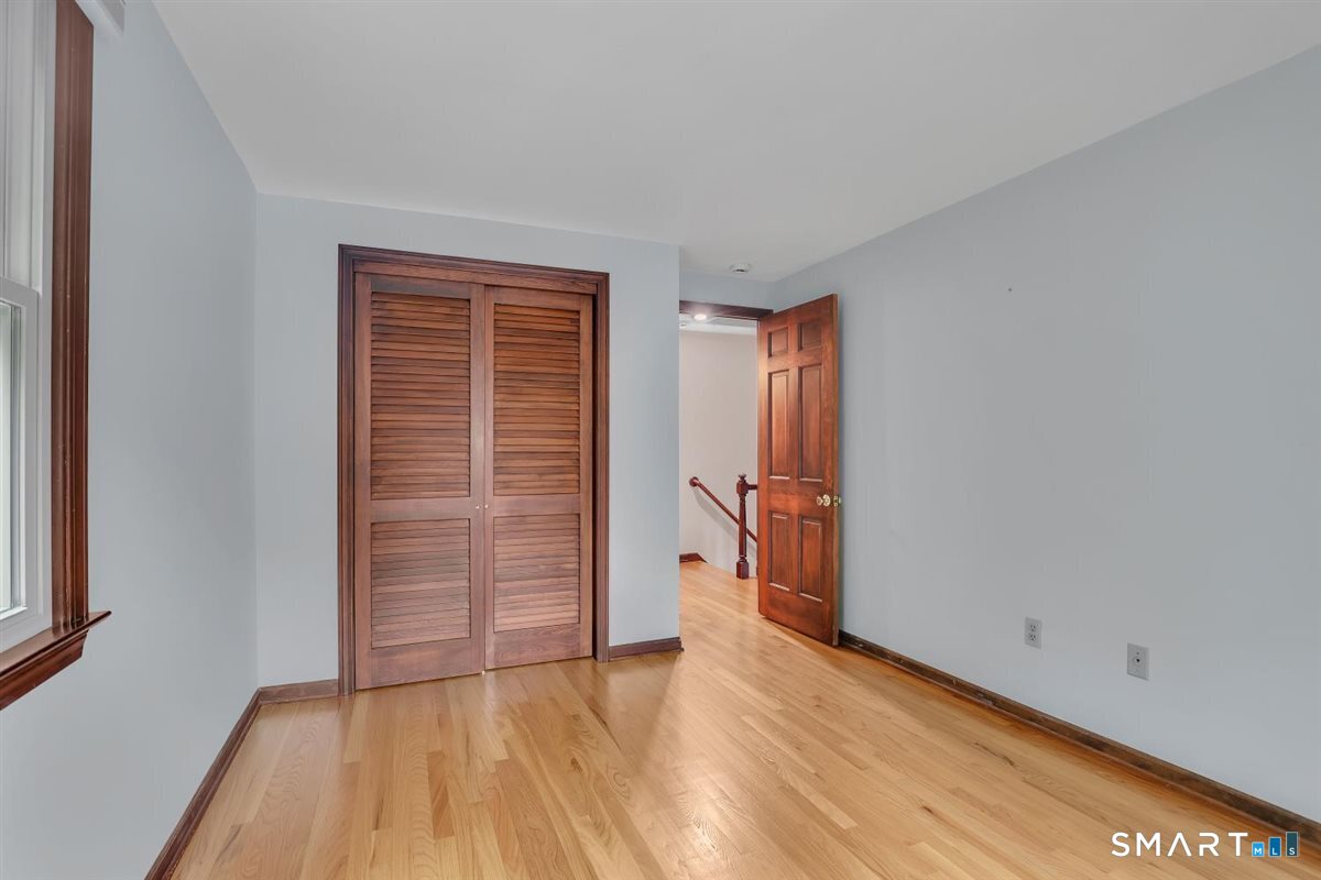 Vacant bedroom with hardwood floors, a louvered closet, and an open doorway to the hall.