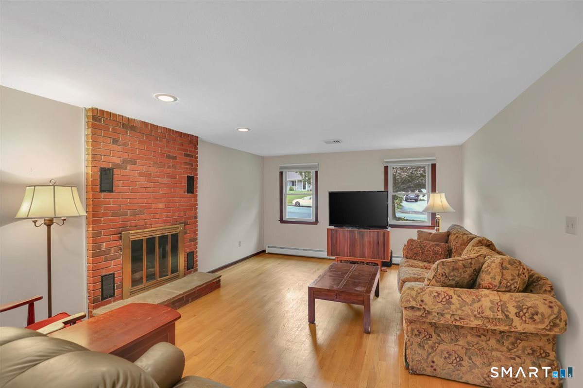 Living room with a brick fireplace, hardwood floors, and patterned sofas.