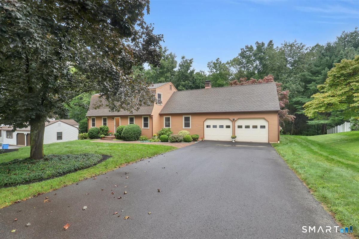 Peach-colored house with an attached two-car garage and a wide driveway, framed by mature trees.