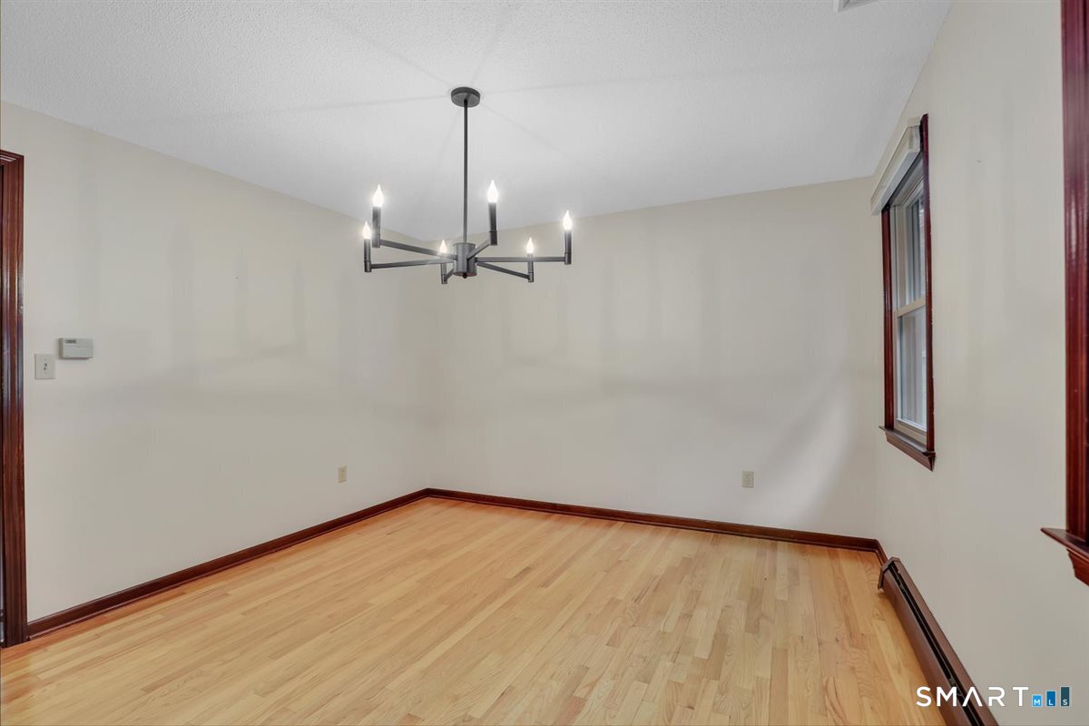 Empty dining room with hardwood floors, dark wood trim, and a modern chandelier.