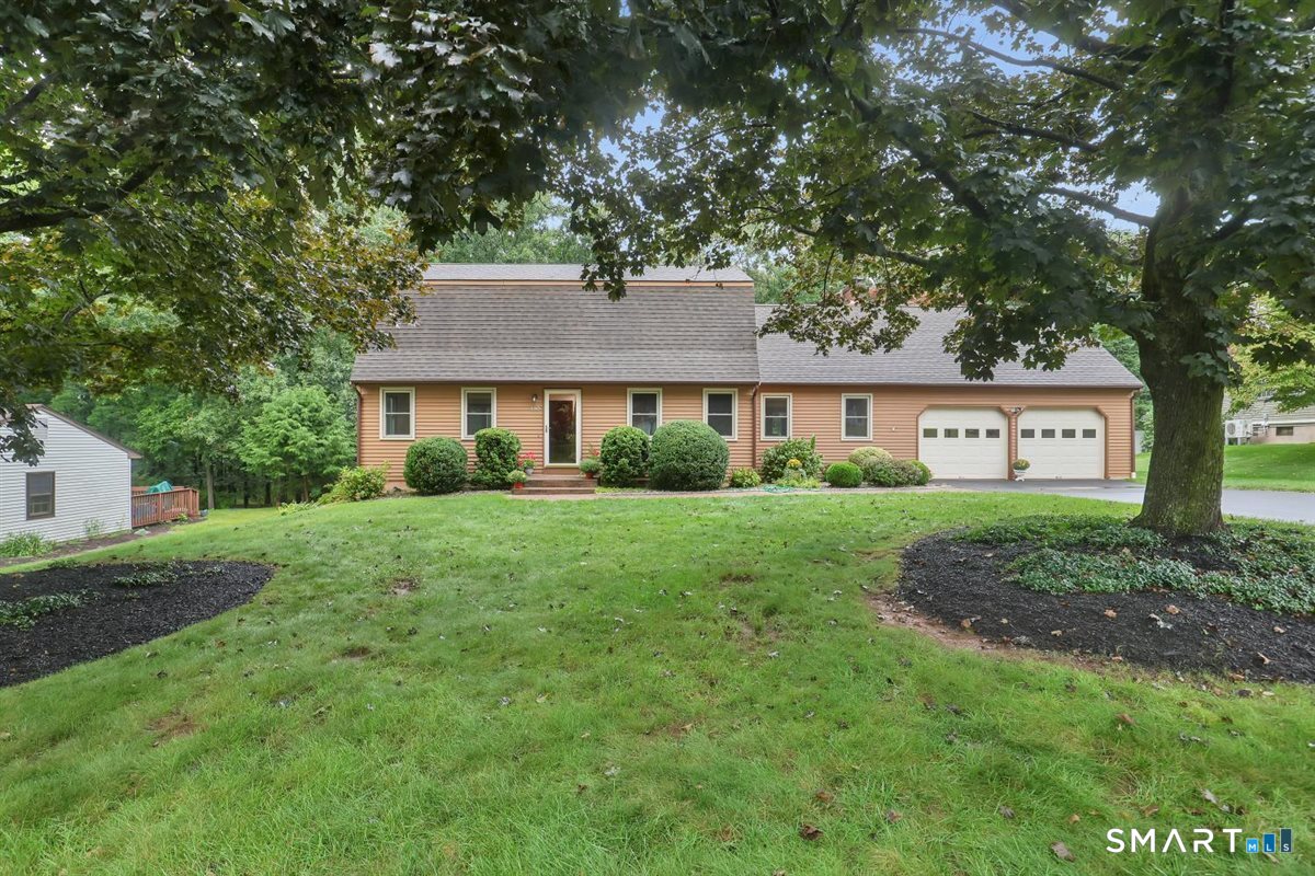 Tan single-story home with an attached two-car garage, framed by mature trees and a broad lawn.