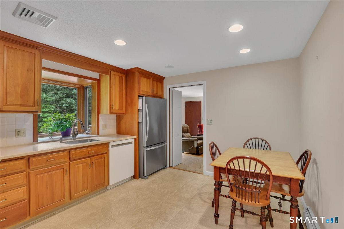 Kitchen and dining area with honey-colored cabinets, stainless steel refrigerator, and wooden dining set.