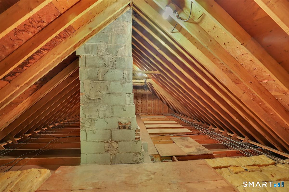 Unfinished attic with exposed rafters, a central block chimney, and loose wiring.