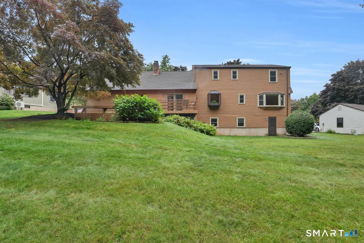 Two-story brown house with a long wooden deck overlooking a broad lawn.