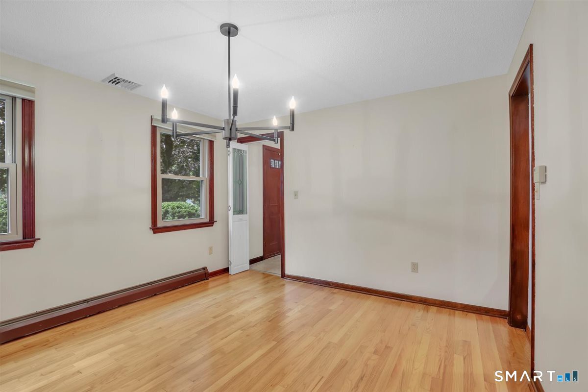 Empty dining room with hardwood floors, dark wood trim, and a modern chandelier.