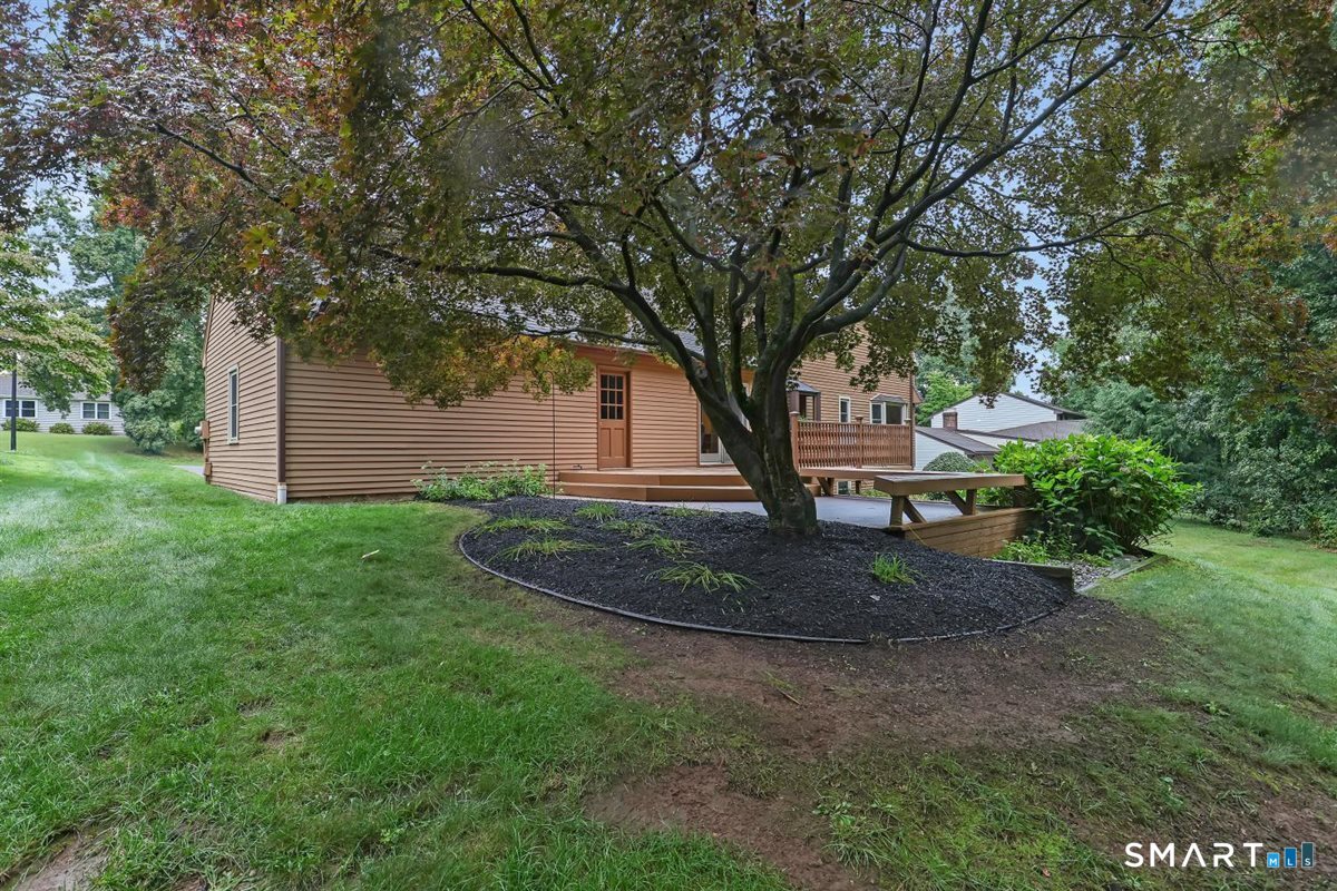 Tan-sided house with a raised wooden deck, large shade tree, and landscaped yard.