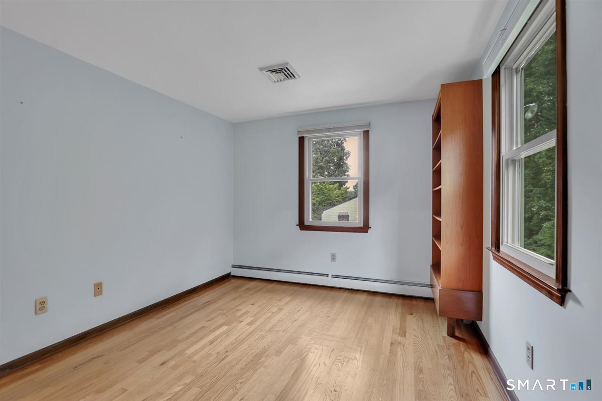 Empty room with hardwood floors, two windows, and a built-in wooden shelving unit.