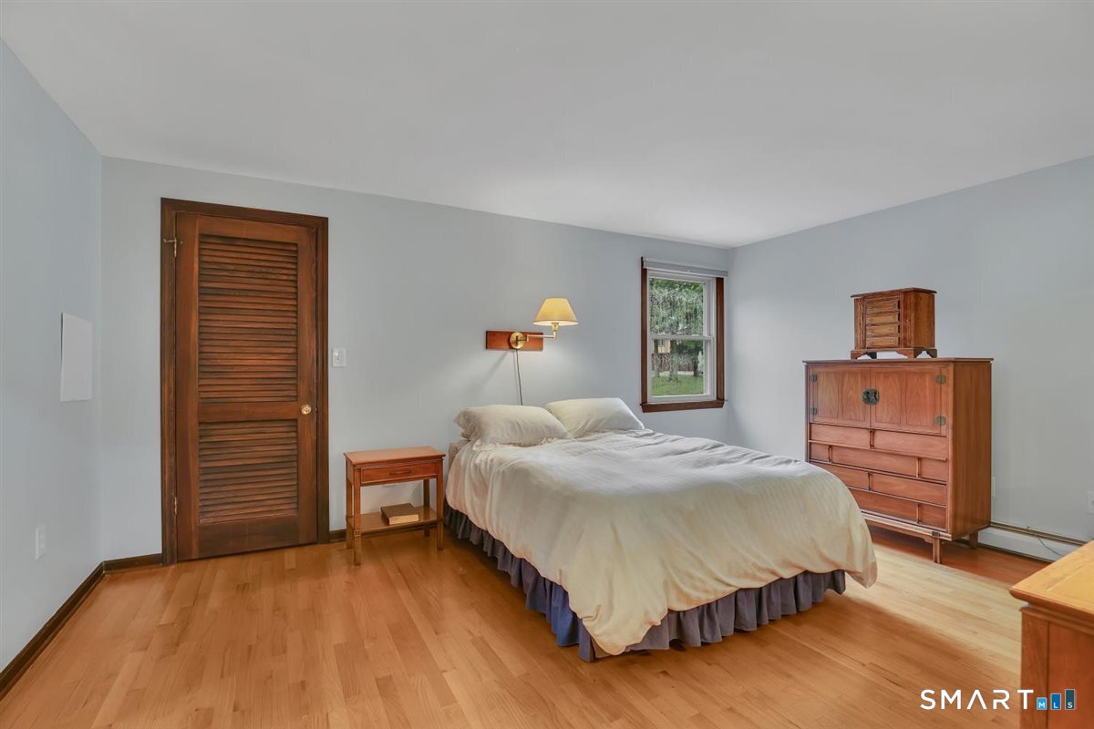 Bedroom with white bedding, warm wood floors, and matching wooden furniture.