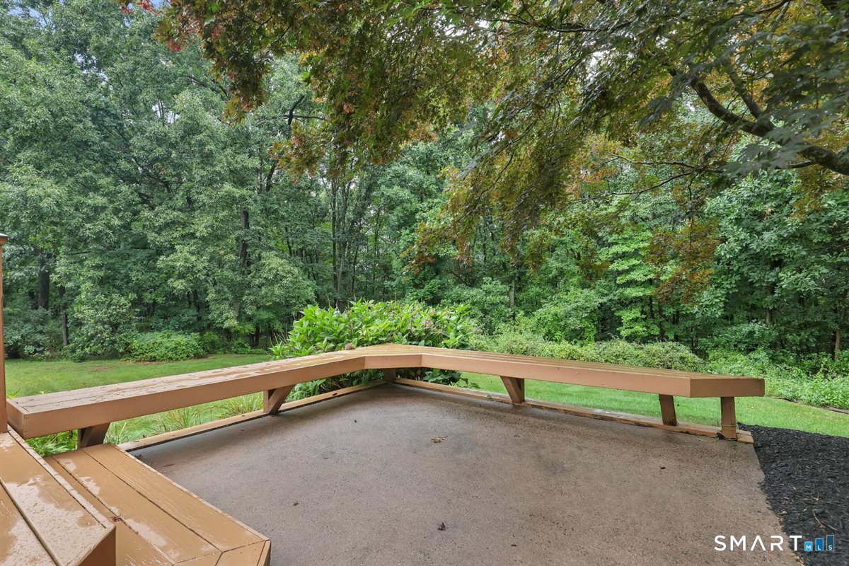 Concrete patio with a wooden railing overlooks a lawn and dense wooded yard.