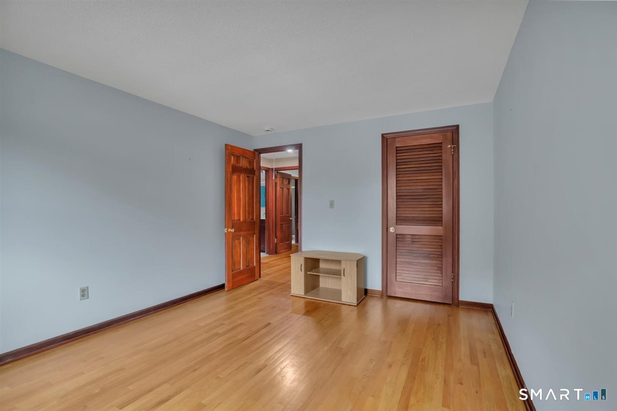 Empty bedroom with hardwood floors, a louvered closet door, and a small table.