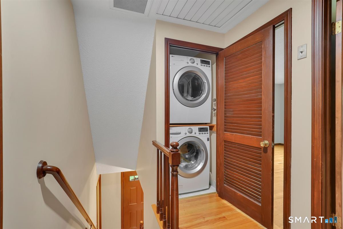 Stacked washer and dryer in an upstairs laundry closet beside a hardwood staircase.