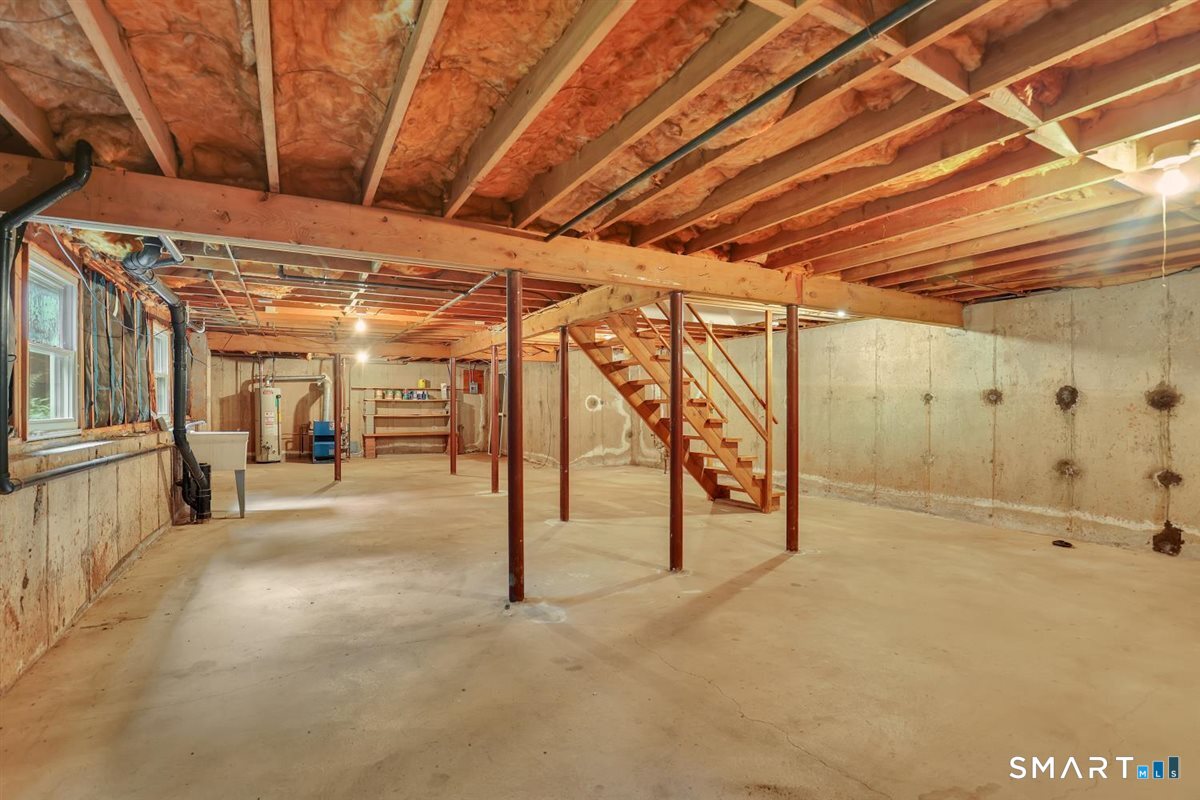 Unfinished basement with exposed ceiling insulation, support posts, and wooden stairs.