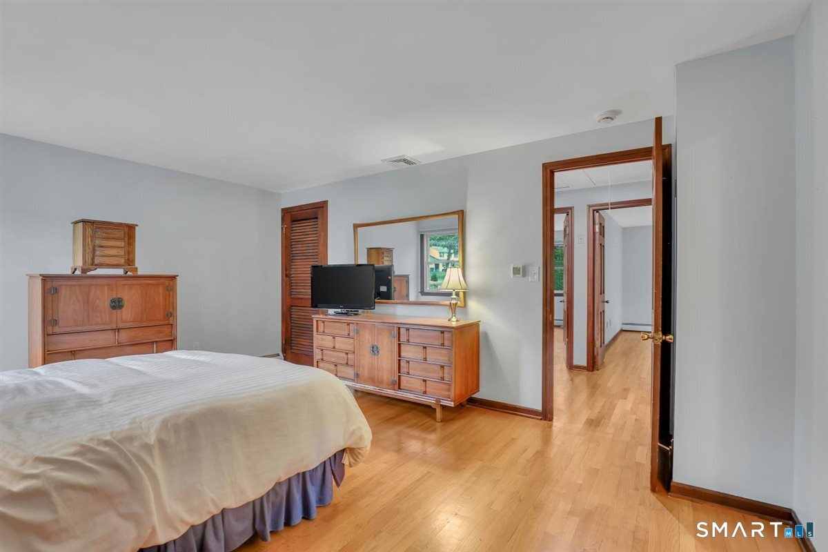 Bedroom with matching wooden dressers, a wall mirror, and hardwood floors.