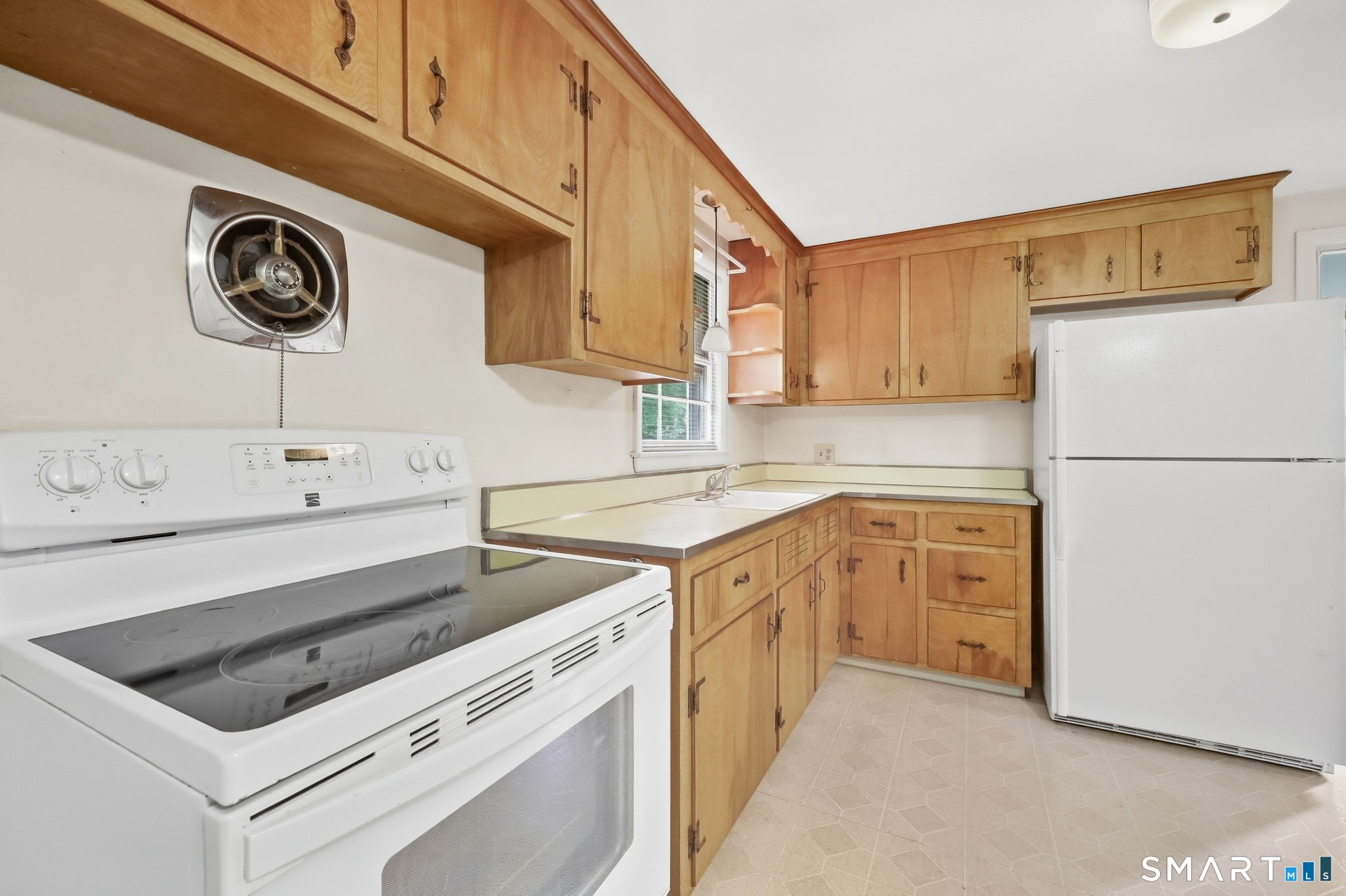 Kitchen with honey-colored cabinets, white appliances, and a sink beneath the window.
