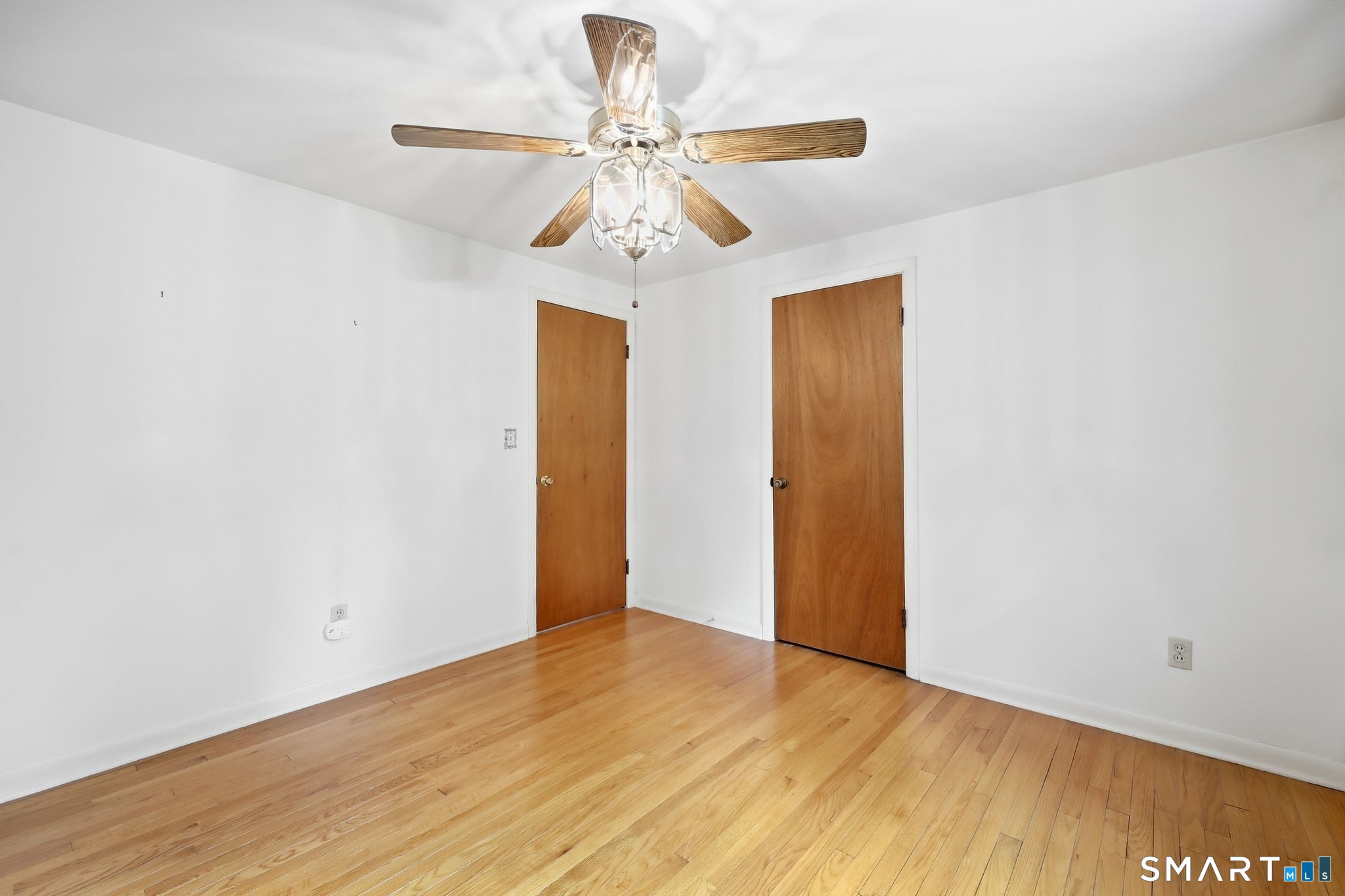 Empty room with hardwood floors, two wooden doors, and a ceiling fan with light.