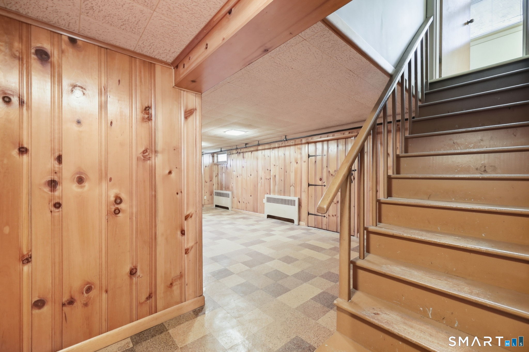 Basement with knotty pine walls, checkered tile floor, and wooden staircase.