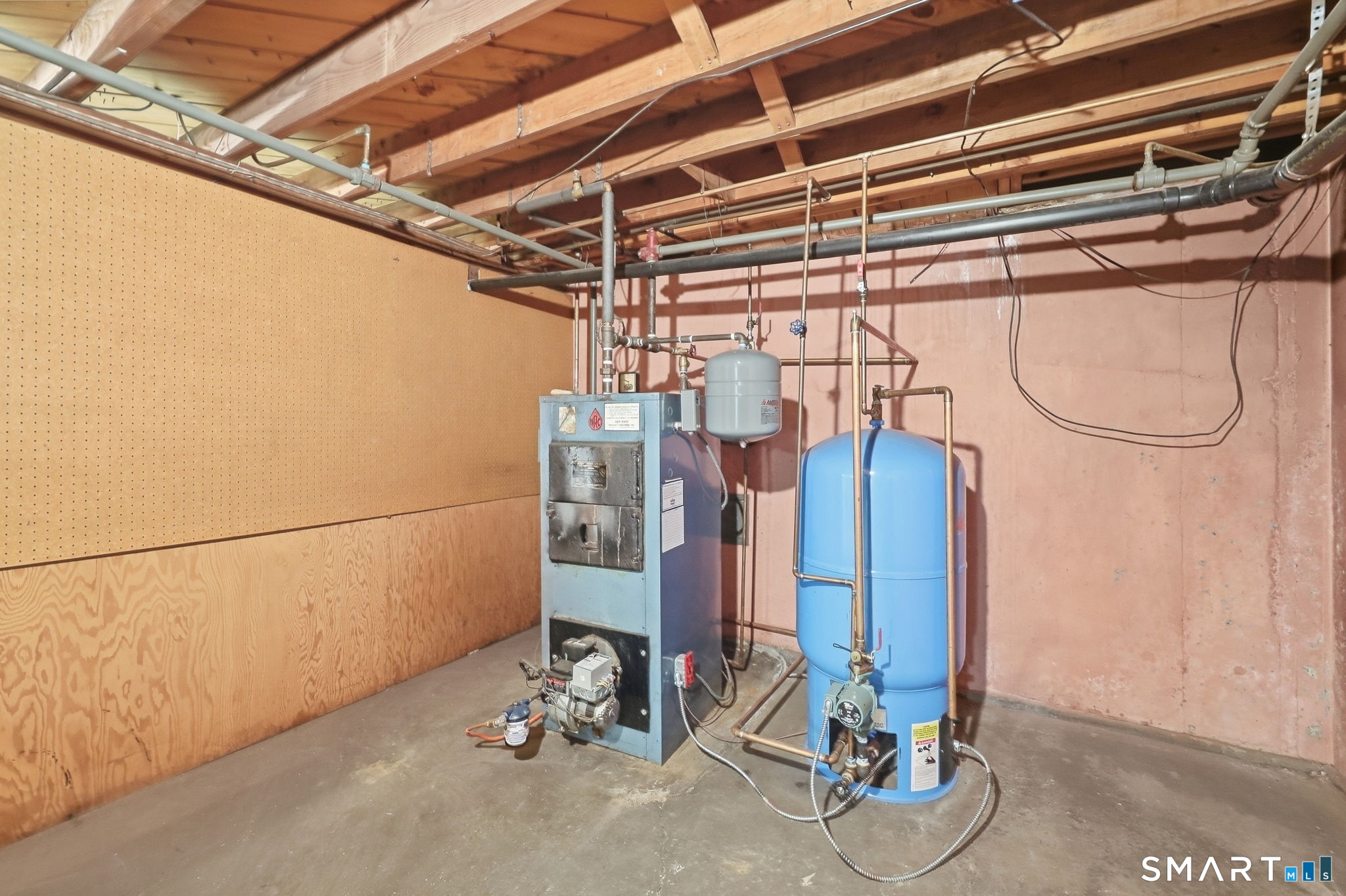 Basement utility room with a boiler, blue pressure tank, and exposed plumbing.