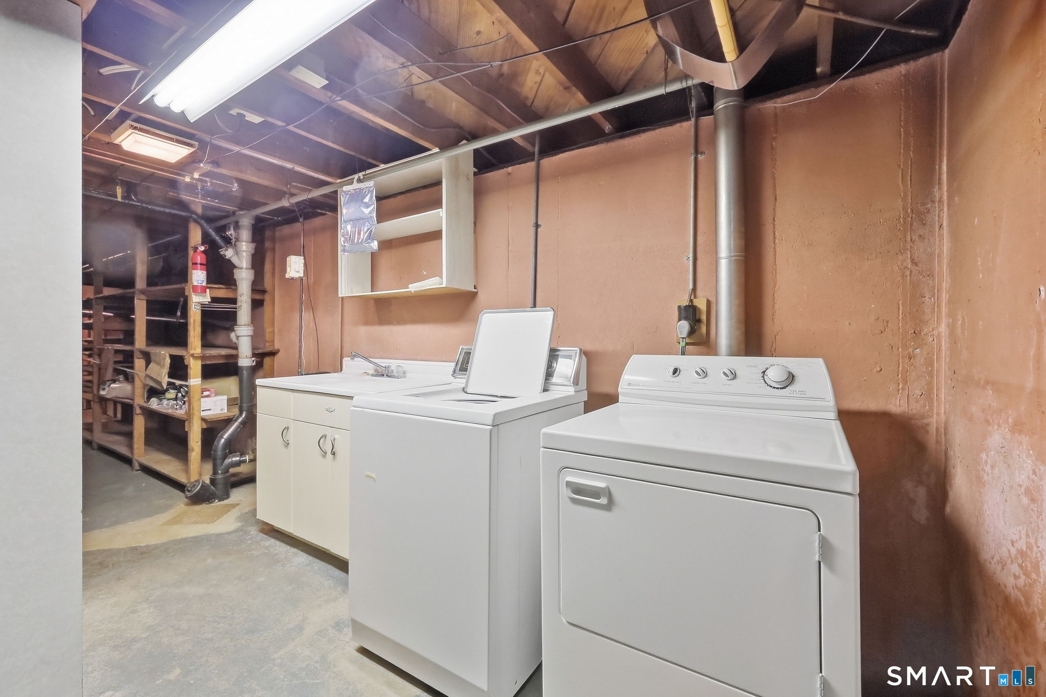 Basement laundry area with washer, dryer, utility sink, and open storage shelves.