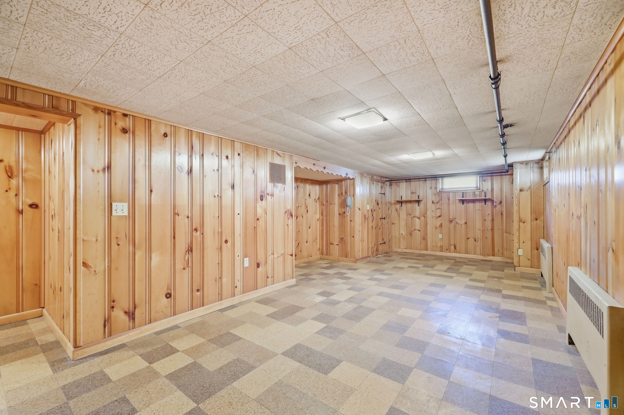 Vacant finished basement with knotty pine walls and a multicolored tile floor.