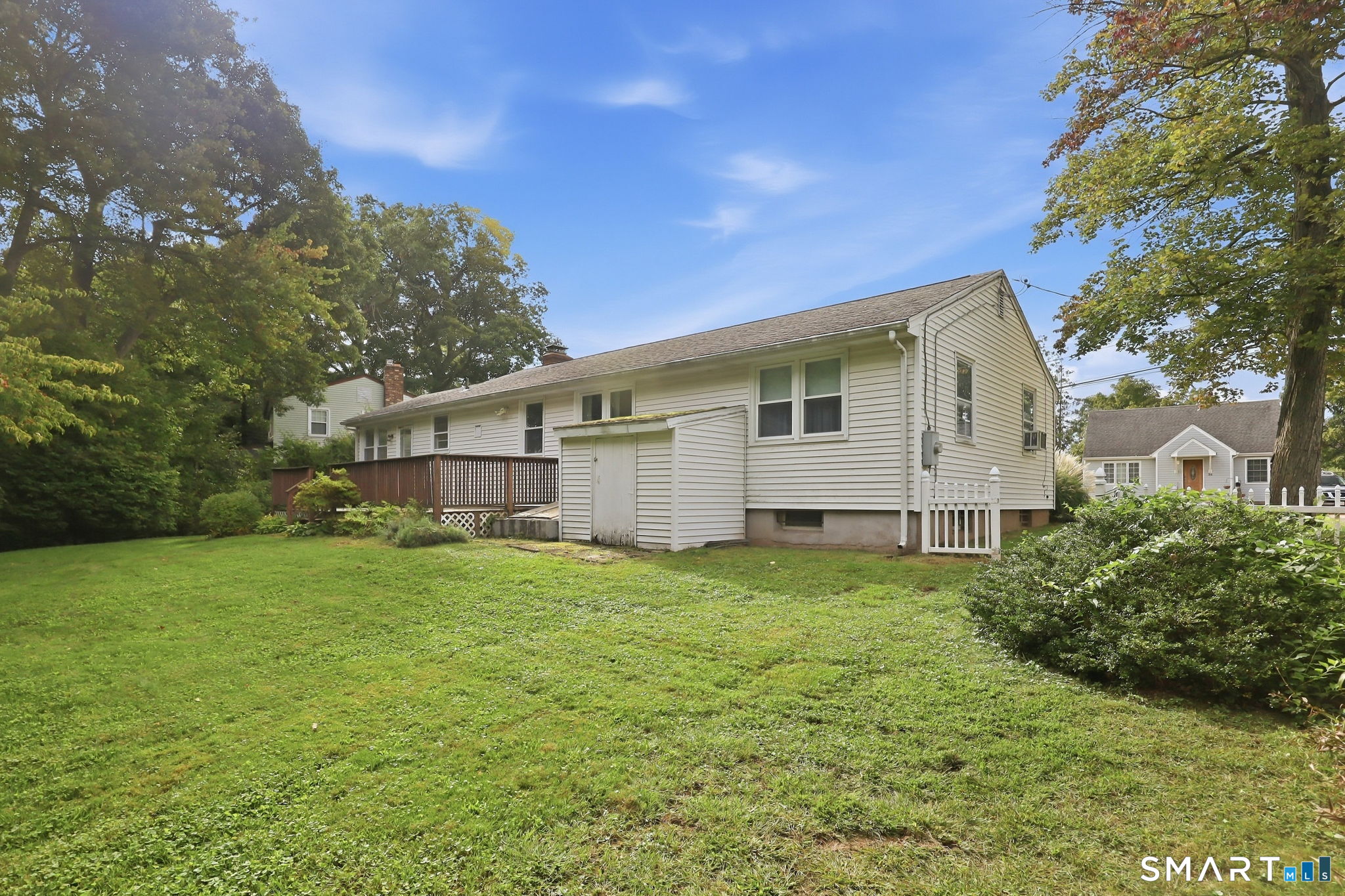 Rear of a single-story house with a wooden deck and broad grassy yard.