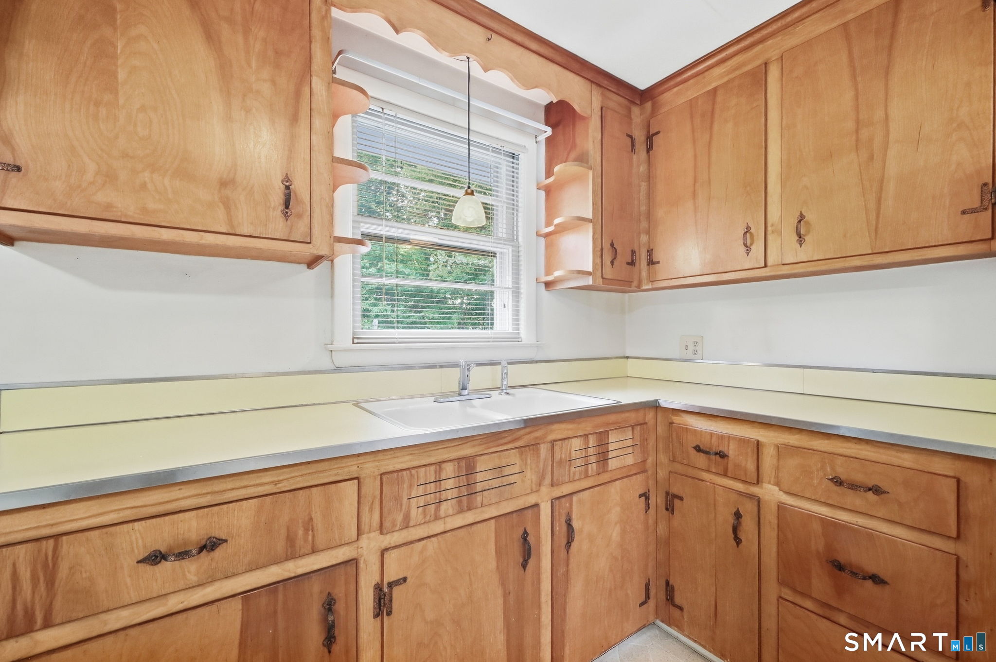 Kitchen with honey-colored wood cabinets, pale yellow counters, and a sink beneath a window.