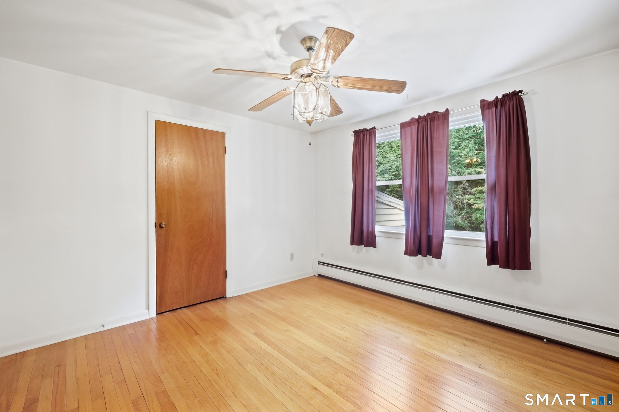 Vacant room with hardwood floors, a ceiling fan, and burgundy curtains framing the window.