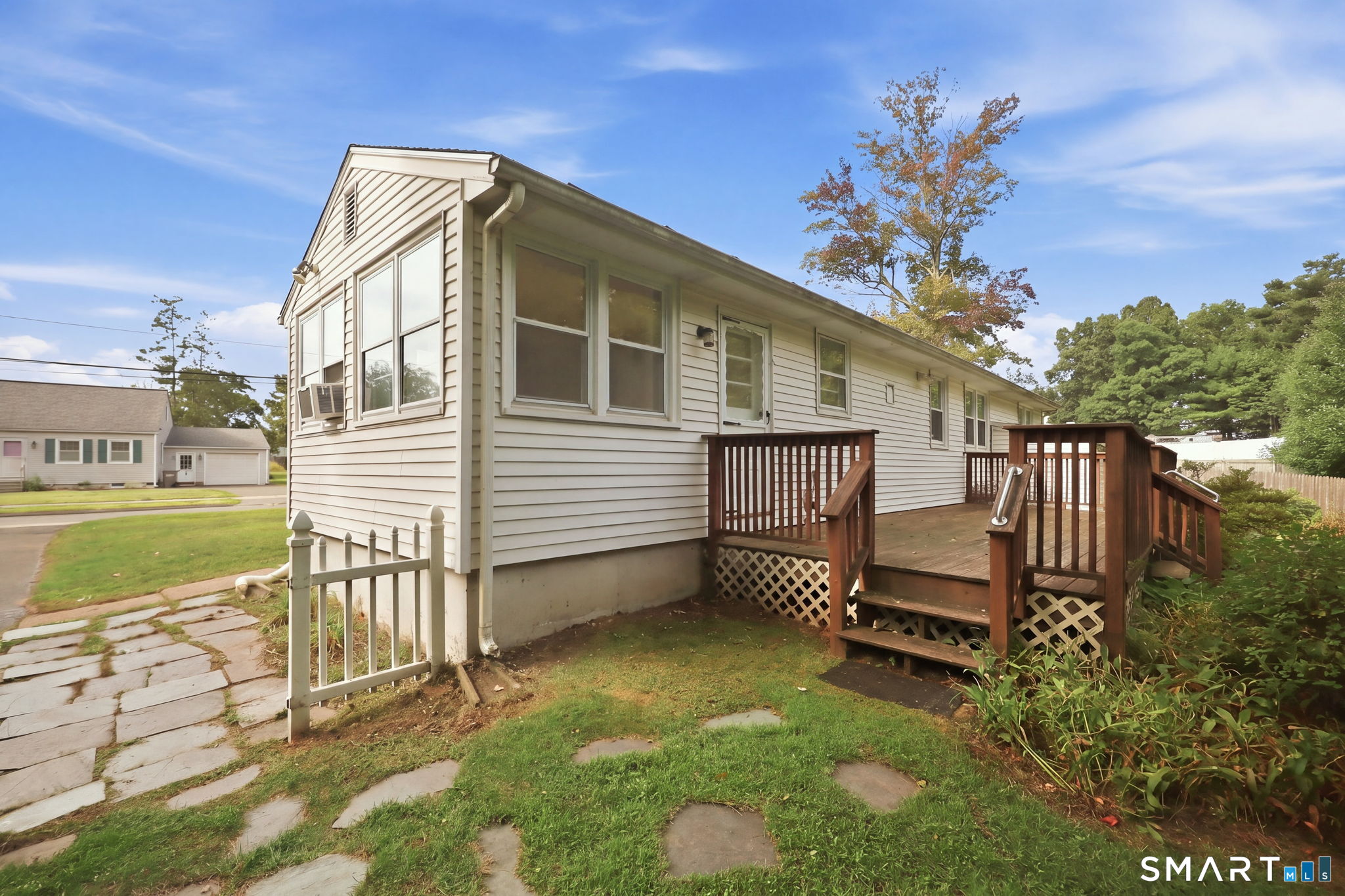Single-story home with light siding and a raised wooden deck beside a stone path.