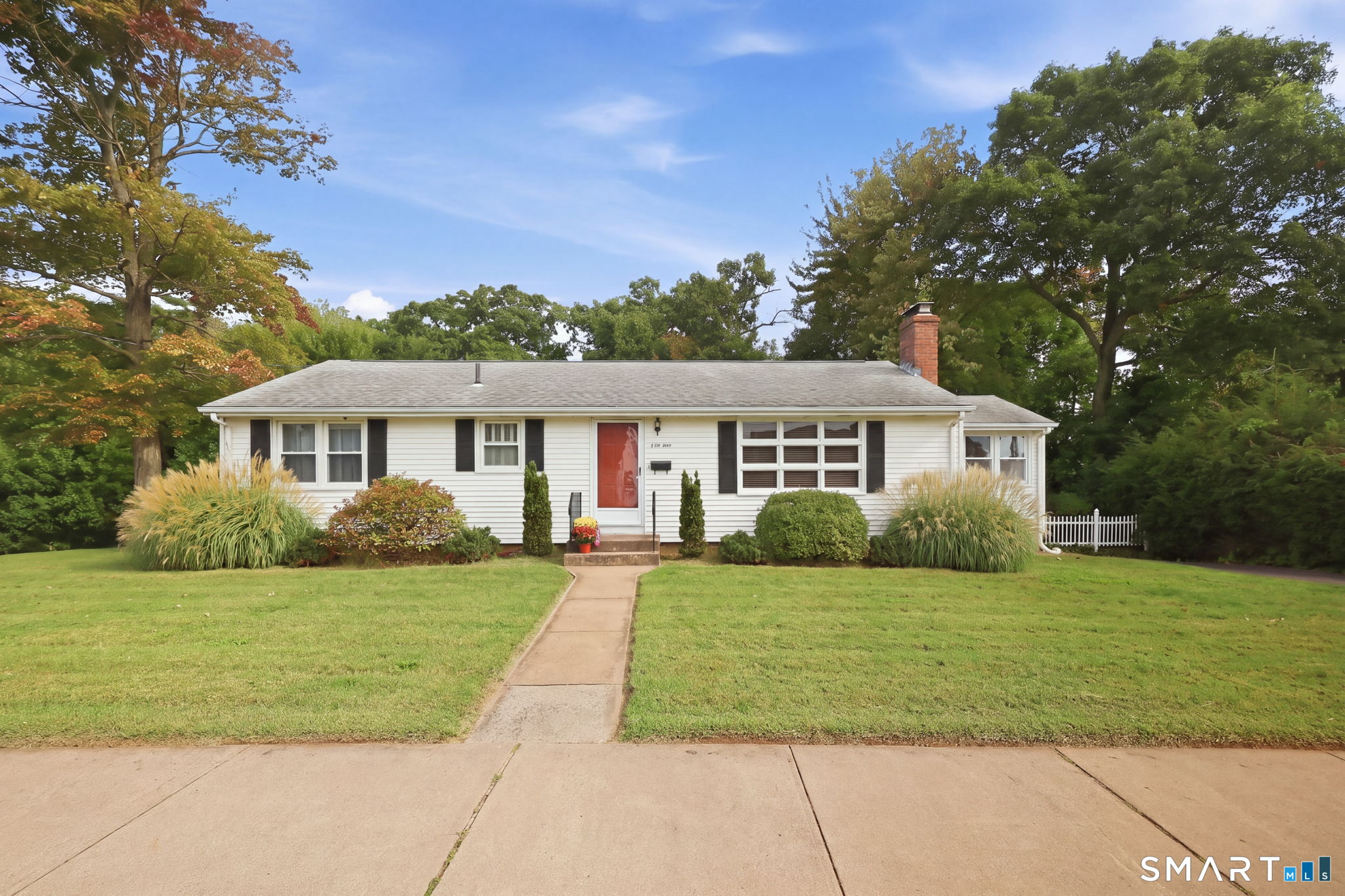 White ranch house with a red front door, brick chimney, and landscaped front lawn.