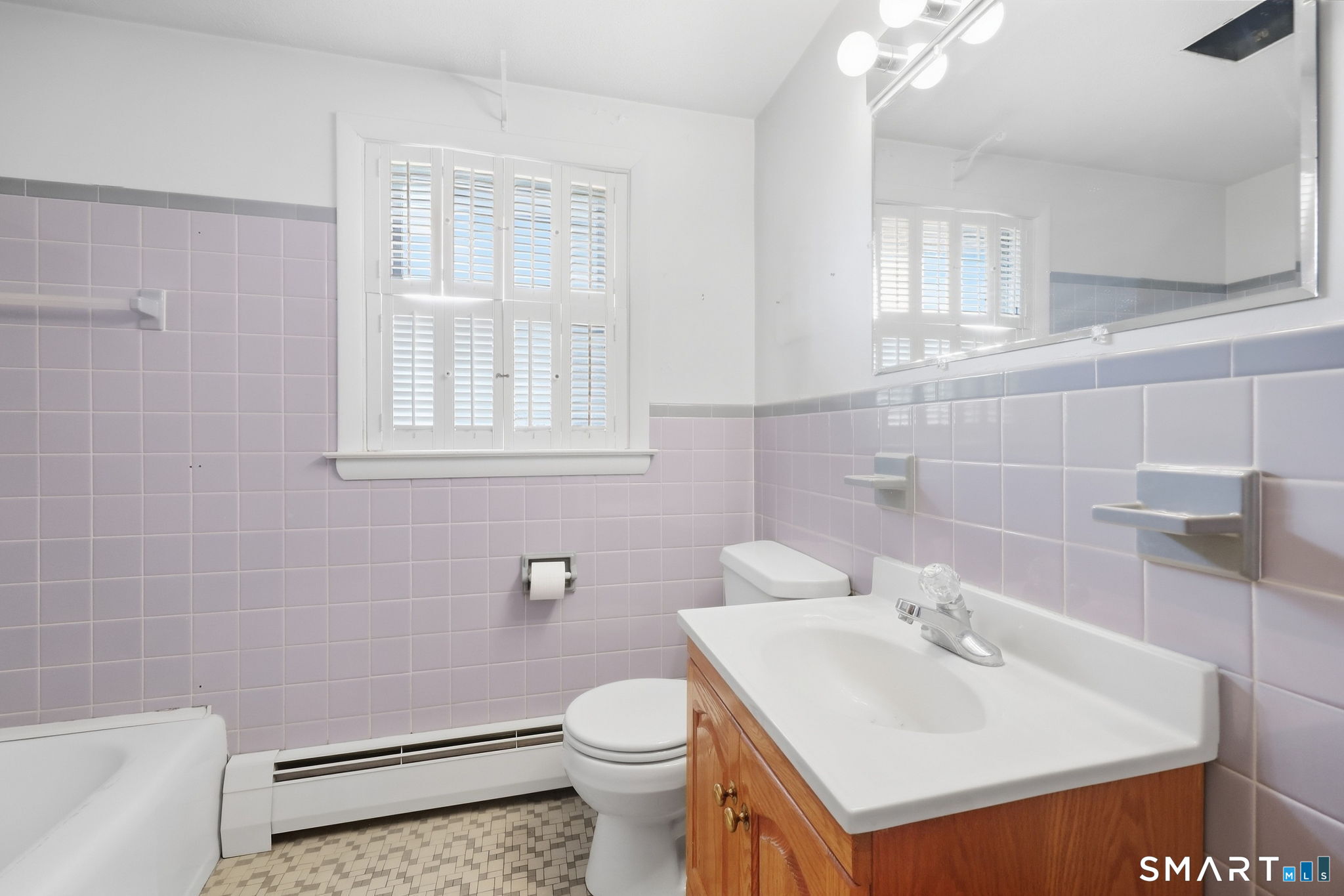 Bathroom with lavender tile, plantation shutters, and a wood vanity beside the bathtub.