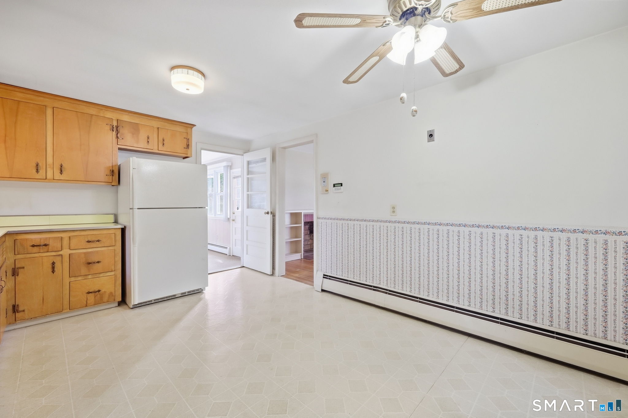 Kitchen with honey-colored cabinets, white refrigerator, patterned wainscoting, and a ceiling fan.
