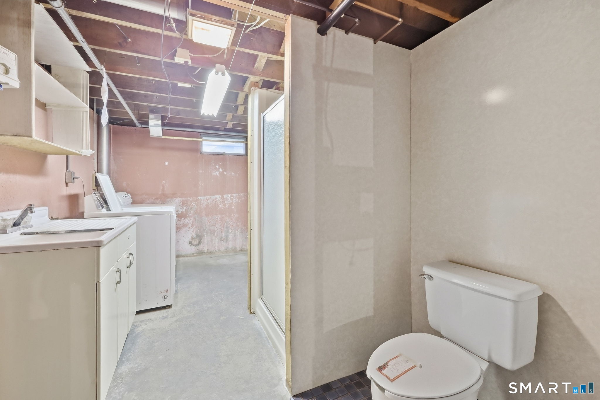 Basement bathroom with a toilet and shower beside a laundry sink and washing machine.