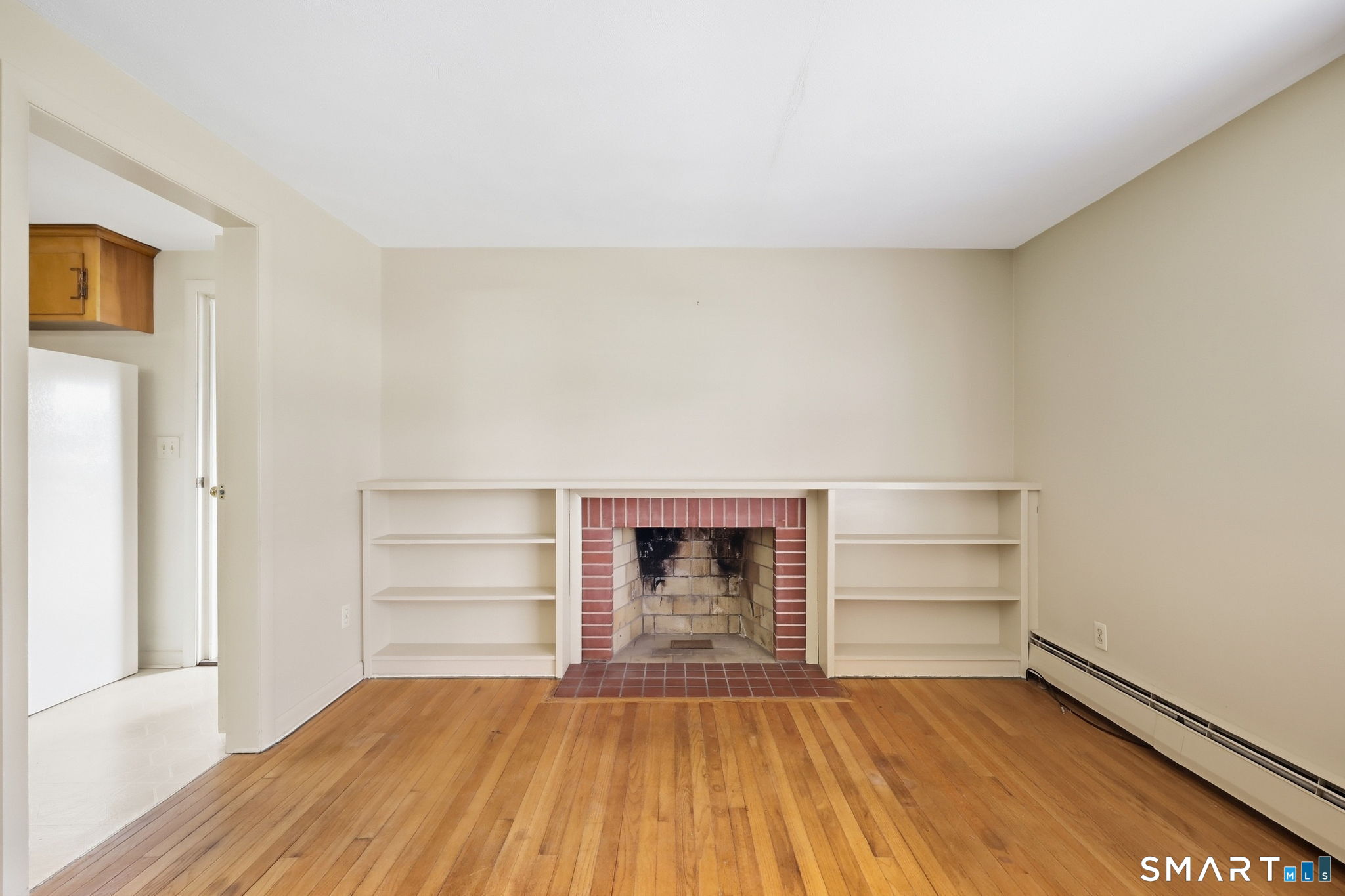 Vacant living room with hardwood floors, a brick fireplace, and built-in shelving.