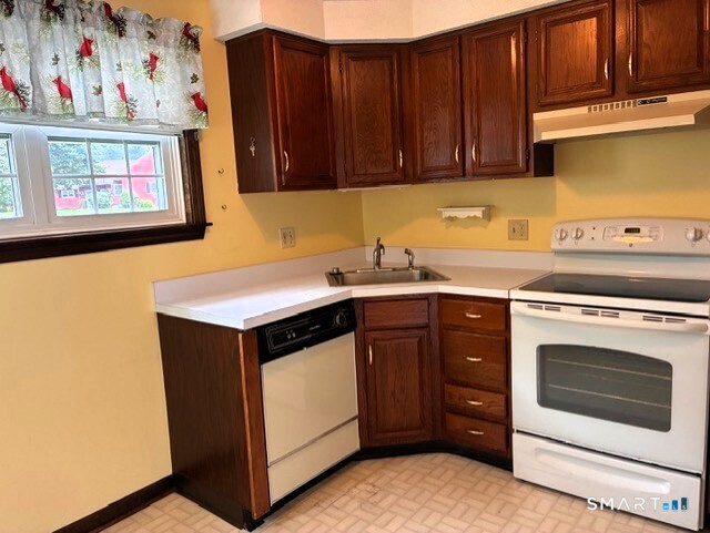 Compact kitchen with dark wood cabinets, white countertops, and a white electric range beside the sink.