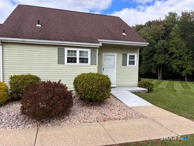 Pale yellow home with a steep brown roof, gravel landscaping, and a walkway leading to the front door.