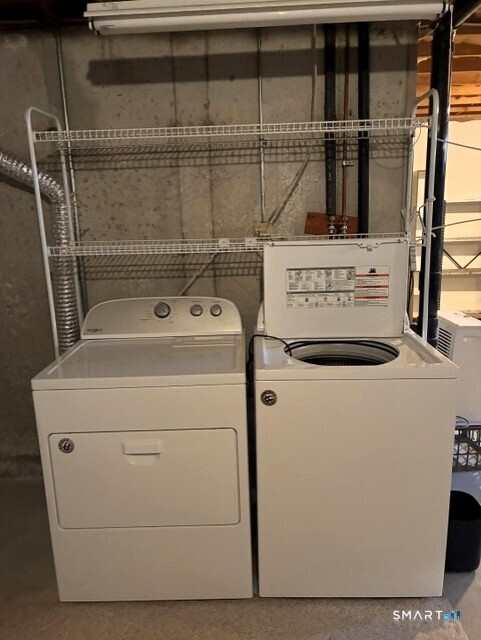 Basement laundry area with a top-load washer and dryer beneath wire shelving.