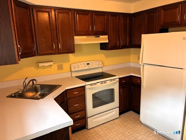 Kitchen with dark wood cabinets, yellow walls, and white appliances.