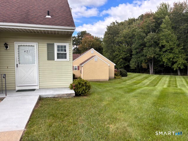 Light green-sided home with a white entry door, yellow detached garage, and striped lawn.