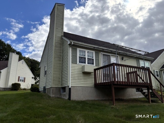 Rear exterior of a light-sided home with a tall chimney and raised wooden deck.