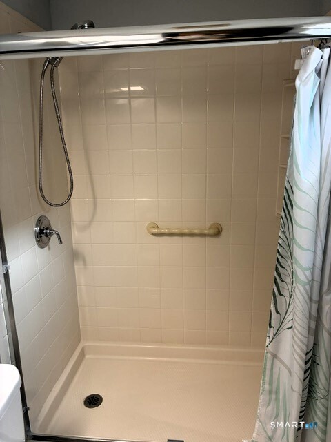 Tiled walk-in shower with a handheld showerhead, grab bar, and patterned curtain.