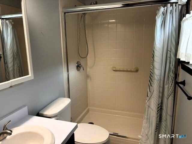 Bathroom with a tiled tub and shower, grab bar, toilet, and white vanity.