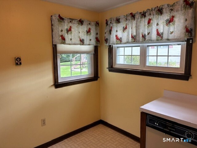 Small yellow kitchen with floral window valances, patterned flooring, and a white countertop beside a black oven.