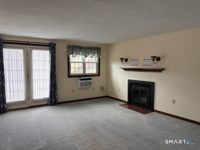 Empty living room with gray carpet, black fireplace, and glass doors beside a window air conditioner.