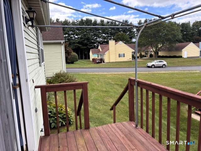 Wooden deck overlooking a lawn, road, and neighboring homes beneath an overhead canopy frame.